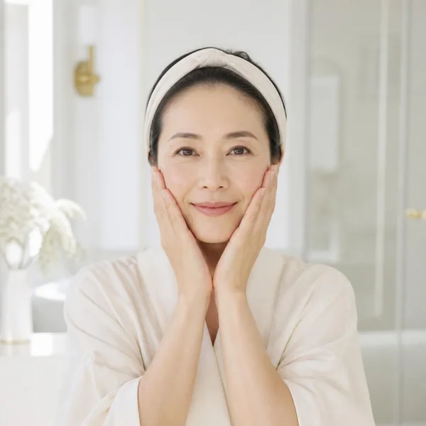 朝の光の中で頬に手を当ててほほえむ女性